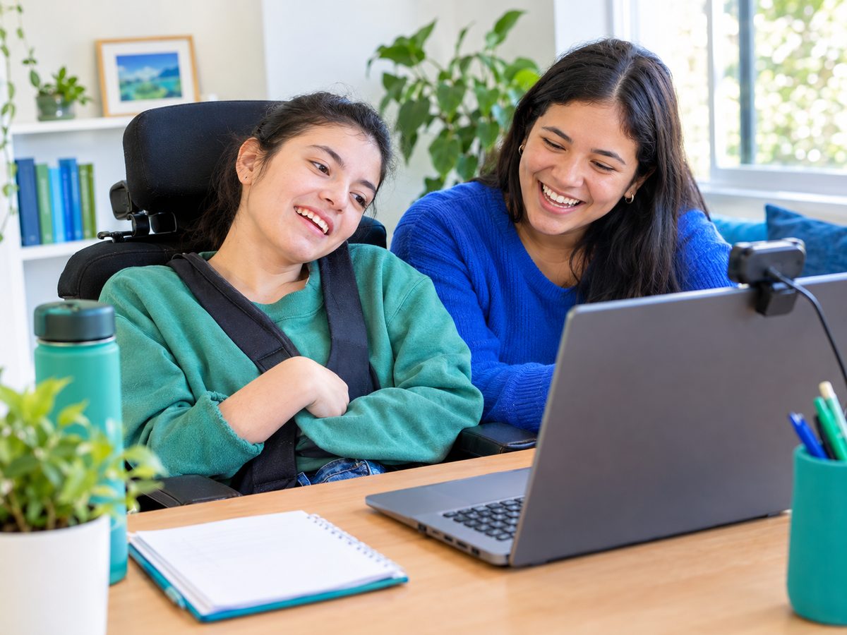 Una joven con parálisis cerebral y una amiga ríen frente a un portátil